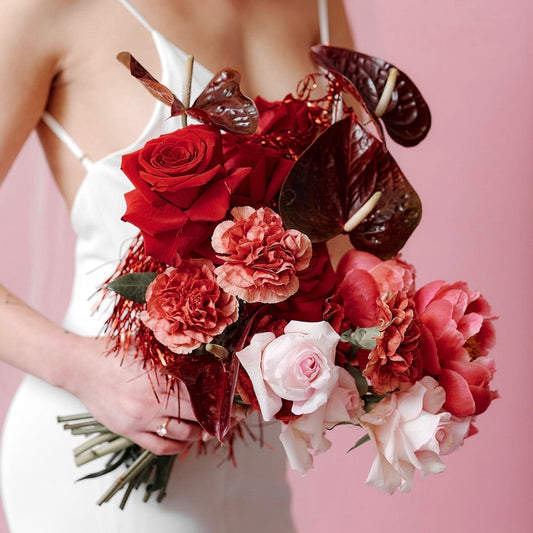 Woman holding a bouquet of red and pink flowers against a pink background